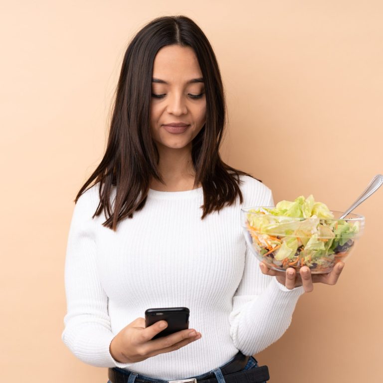young-brunette-woman-holding-salad-sending-message-with-mobile (1)